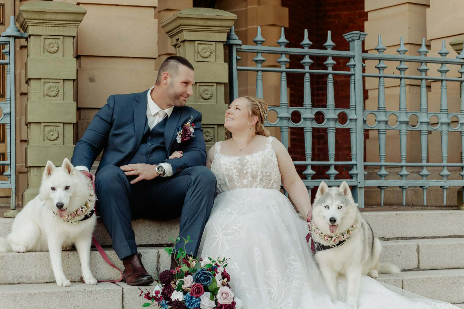 Bride and groom seated with their two huskies wearing flower collars